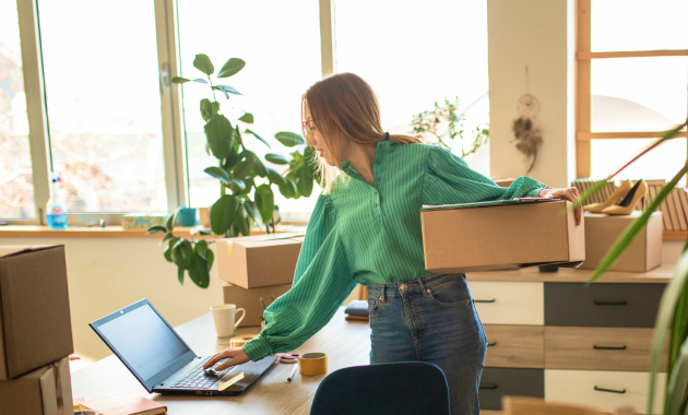Chủ shop online kiểm tra đơn hàng trên laptop giữa các thùng hàng