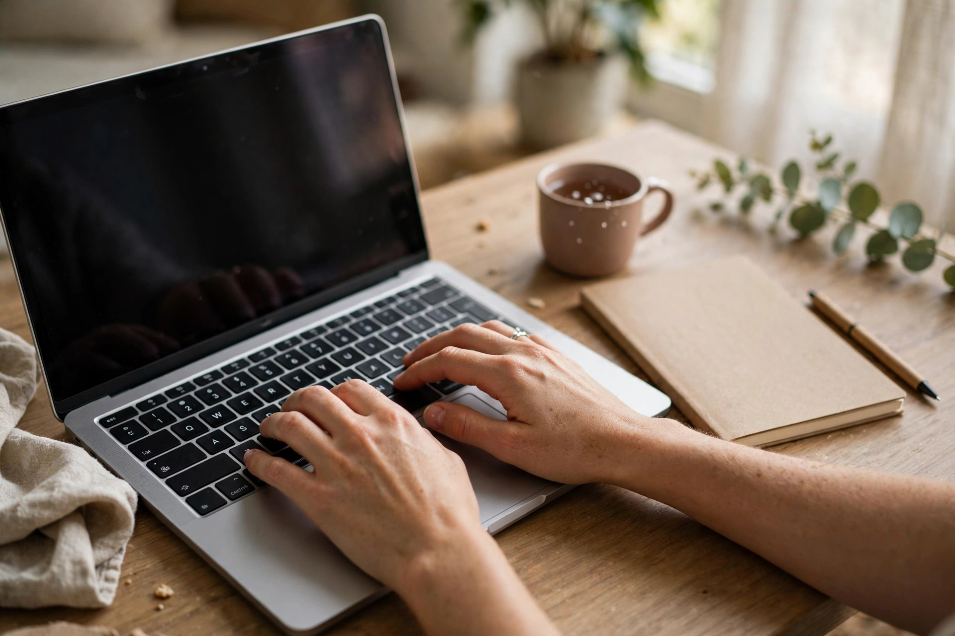 Bàn tay gõ bàn phím laptop bên cạnh sổ tay và bút để soạn thư xin việc