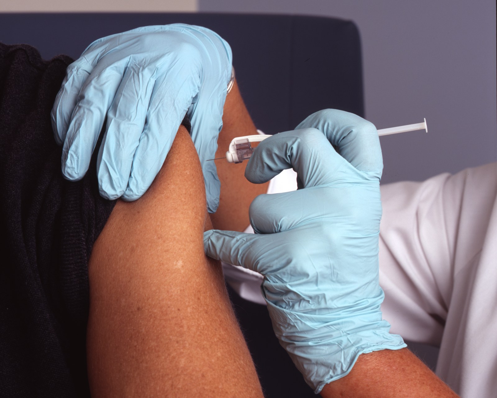 Nhân viên y tế đeo găng tay tiêm vaccine vào bắp tay bệnh nhân